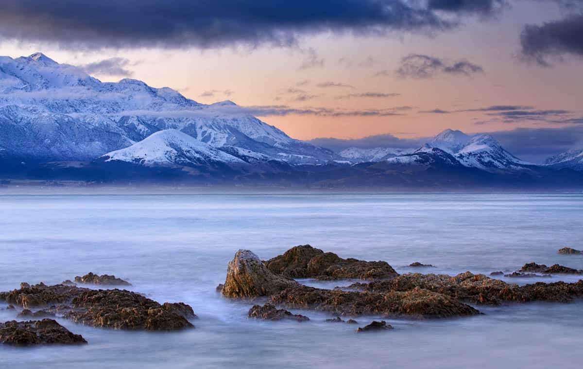Evening light warms snowy peaks beside Kaikōura, New Zealand.